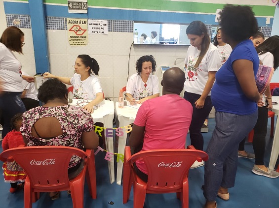 #pracegover na imagem há duas agentes de saúde sentadas à uma mesa conversando com duas pessoas na escola de samba